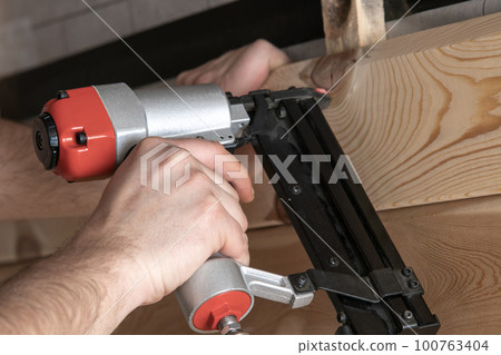 Unrecognizable male hands use stapler, nail gun for wooden timber board, fasten metal nail. Woodworking and handicraft Unrecognizable male hands use stapler, nail gun for wooden timber board, fasten metal nail. Woodworking and handicraft 100763404