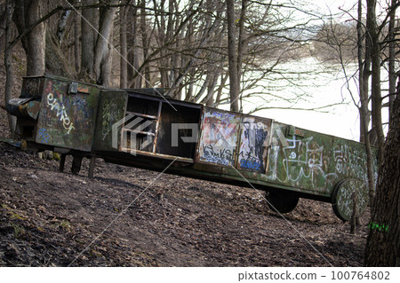 Rusty vintage train carriage abandoned on the hill in the forest near river. Covered in written graffiti drawings metal transport of old times. 100764802