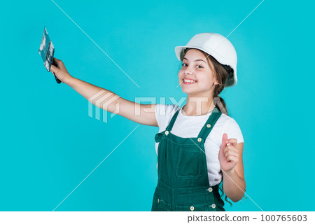 confident kid use spatula while repairing. concept of building and renovation. happy girl use spatula tool. teen builder wear safety helmet. young worker in protective hard hat confident kid use spatula while repairing. concept of building and renovation. happy girl use spatula tool. teen builder wear safety helmet. young worker in protective hard hat 100765603