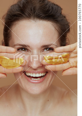 smiling young woman with eye patches on beige background 100765770