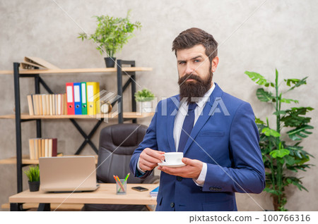 confident bearded businessman drinking coffee in the office with copy space, coffee break 100766316