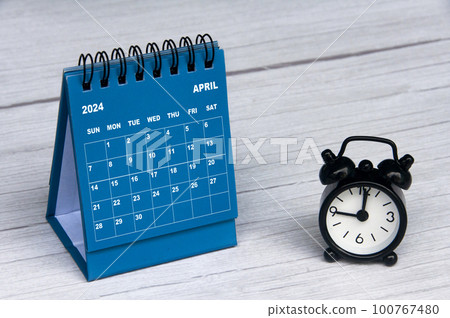 April 2024 calendar on wooden desk and alarm clock with customizable space for text. Monthly calendar concept and copy space. 100767480