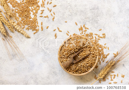 Bowl of raw dry rye grain with a wooden spoon on white table top view 100768538
