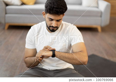 Arabic man setting heart-rate watch during home training Arabic man setting heart-rate watch during home training 100769066