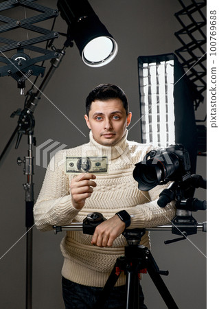 photographer with digital camera on tripod holding hundred dollar bills 100769688