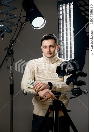 photographer with digital camera on tripod holding hundred dollar bills 100769689