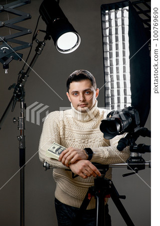 photographer with digital camera on tripod holding hundred dollar bills 100769690