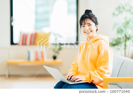 A young woman using a laptop in her living room. 100771040
