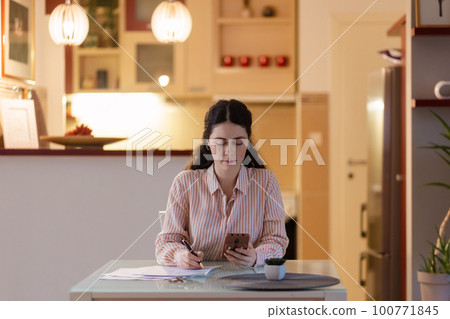 Freelance and remote work. Young beautiful Caucasian woman is sitting at table and using smartphone. Electric light. Concept of social networks and Internet search Freelance and remote work. Young beautiful Caucasian woman is sitting at table and using smartphone. Electric light. Concept of social networks and Internet search 100771845