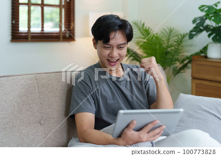 Portrait of an Asian teenager using a digital tablet on the sofa while relaxing at home. 100773828