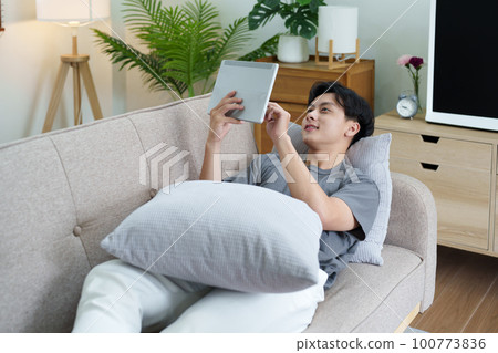 Portrait of an Asian teenager using a digital tablet on the sofa while relaxing at home. Portrait of an Asian teenager using a digital tablet on the sofa while relaxing at home. 100773836