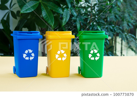 Blue, yellow and green tank for separate garbage collection against bacground with green plants, waste recycling and conservation of the environment concept 100773870
