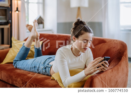 Young woman scrolling her smartphone in the apartment. 100774530