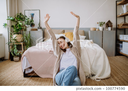 Young woman listening music trough headphones in her apartment. 100774590