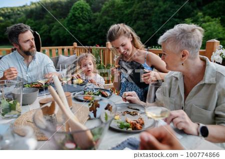 Multigenerational family eating dinner at barbecue party. 100774866