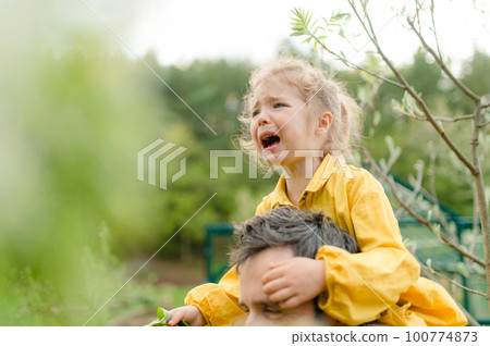 Father holding his crying little daughter and comforting her in garden Father holding his crying little daughter and comforting her in garden 100774873