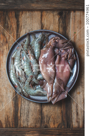 Raw seafood. Fresh shrimps and squids on gray plate. Wooden backround. 100774961
