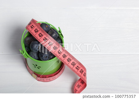 Large blueberries in a decorative bucket. Measuring tape for measuring the waist. International day without diets. Close-up. Large blueberries in a decorative bucket. Measuring tape for measuring the waist. International day without diets. Close-up. 100775357
