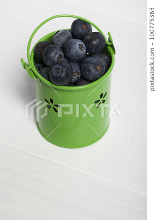 Light green decorative bucket with large blueberries. International day without diets. On a white background. Close-up. 100775363