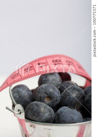 Large blueberries in a decorative bucket. Measuring tape for measuring the waist. International day without diets. On a white background. Close-up. 100775371