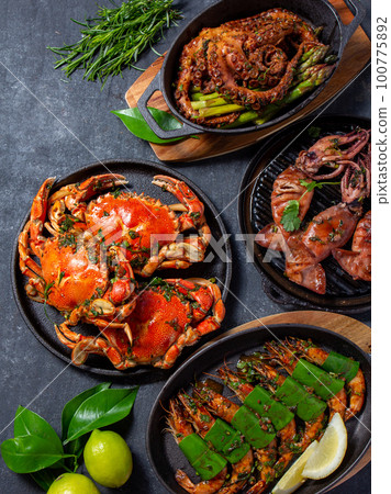 Set of Seafood Dishes. Crabs, octopus, squids and tiger shrimps on cast iron pans and plates on a black background. Top view. 100775892