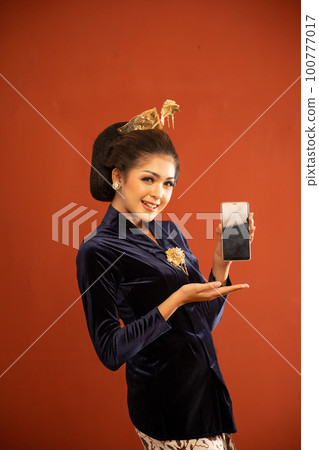 javanese woman in navy kebaya showing the blank phone on isolated background 100777017