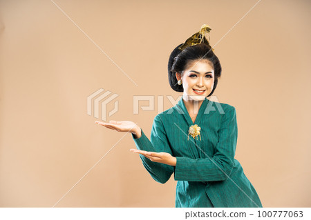 woman in kebaya standing and pointing with her both hands 100777063