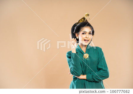 beautiful javanese woman in green kebaya standing looking up with pointed finger 100777082