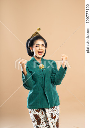 excited woman in green kebaya closing her eyes while clenching her arms 100777100