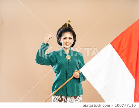 beautiful woman in kebaya standing with clenched arm and holding the flag beautiful woman in kebaya standing with clenched arm and holding the flag 100777110