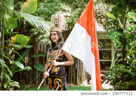 woman in traditional clothes standing with smile while holding the indonesian flag 100777111
