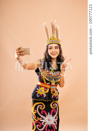 woman in king bibinge standing with peace hand gesture and smiling while taking selfie 100777123