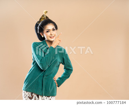 smiling woman in green kebaya looking and pointing on her left side 100777184