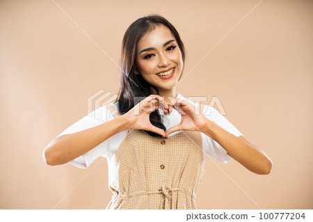 smiling asian woman in casual clothes standing with love hand gesture smiling asian woman in casual clothes standing with love hand gesture 100777204