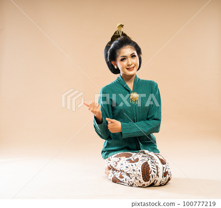 beautiful woman in green kebaya sitting on the floor and pointing 100777219