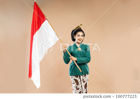 woman in kebaya standing with smile while holding the indonesian flag 100777223
