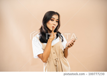 asian woman closing her mouth using her finger while holding the phone asian woman closing her mouth using her finger while holding the phone 100777230