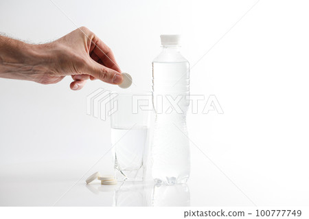 A hand holding effervescent vitamin C is placed in a glass of water. A hand holding effervescent vitamin C is placed in a glass of water. 100777749