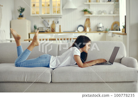 Cute preteen 12s girl use laptop lying on couch 100778235