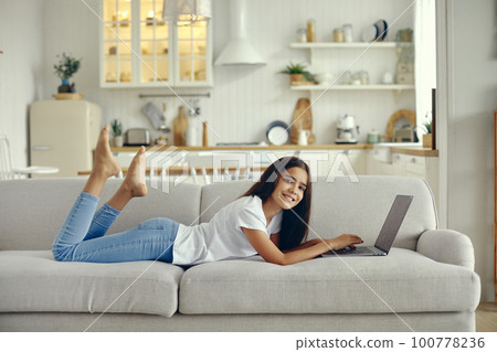 Cute preteen 12s girl use laptop lying on couch 100778236