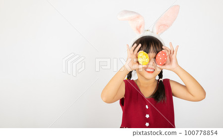 Happy Easter Day. Smile Asian little girl wearing easter bunny ears holding colorfull eggs closes eyes with testicles isolated on white background with copy space, Happy child in holiday 100778854