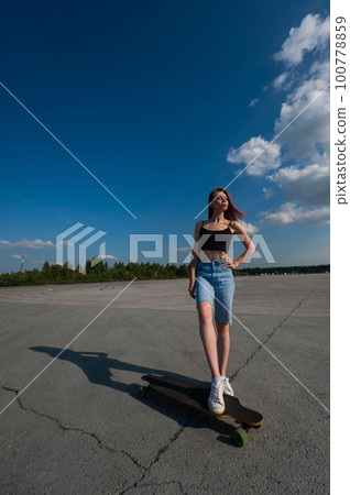 Young caucasian woman riding a longboard outdoors.  100778859