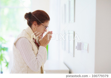 Woman adjusting thermostat. Central heating. 100779379
