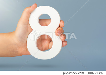 Eight in hand. A hand holds a white number 8 on a blue background. Concept with number eight. Birthday 8 years, percentage, eighth grade or day, international women's day. 100779392