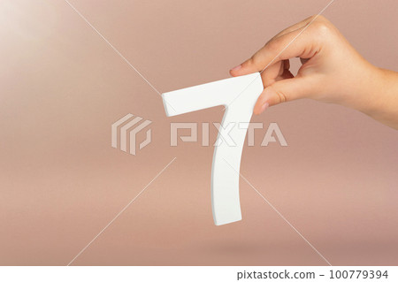 Number seven in hand. Hand holding white number 7 on red background with copy space. Concept with number seven. Birthday 7 years, percent, seventh grade or day. Number seven in hand. Hand holding white number 7 on red background with copy space. Concept with number seven. Birthday 7 years, percent, seventh grade or day. 100779394