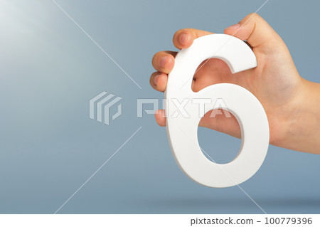 Number six in hand. A hand holds a white number 6 on a blue background with copy space. Concept with number six. 6 percent, birthday 6, sixth grade, in sixth grade Number six in hand. A hand holds a white number 6 on a blue background with copy space. Concept with number six. 6 percent, birthday 6, sixth grade, in sixth grade 100779396