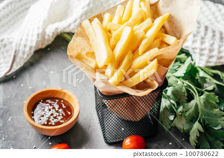 Large serving of French fries stand in craft paper with barbecue sauce, sesame seeds, cherry tomatoes and green parsley 100780622