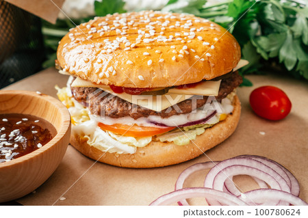 Classic double burger with meat cutlet, lettuce, tomato, pickled cucumber, cheese, onion and sauce on craft paper 100780624