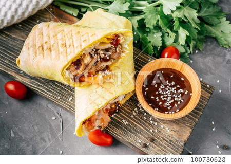 Roll shawarma with sesame seeds, barbecue sauce, chicken in pita bread on wooden surface with cherry tomatoes, parsley Roll shawarma with sesame seeds, barbecue sauce, chicken in pita bread on wooden surface with cherry tomatoes, parsley 100780628
