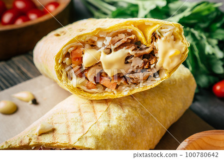 Cheese shawarma with cheese sauce, chicken and vegetables in pita bread on wooden surface, cherry tomatoes and parsley Cheese shawarma with cheese sauce, chicken and vegetables in pita bread on wooden surface, cherry tomatoes and parsley 100780642